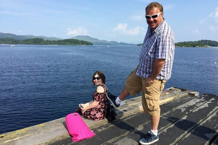Two people on a dock by a lake with mountains in the background. 3
