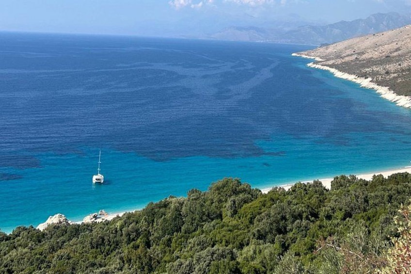 Un paysage côtier avec une mer bleue et limpide, un bateau blanc et une colline boisée. 1