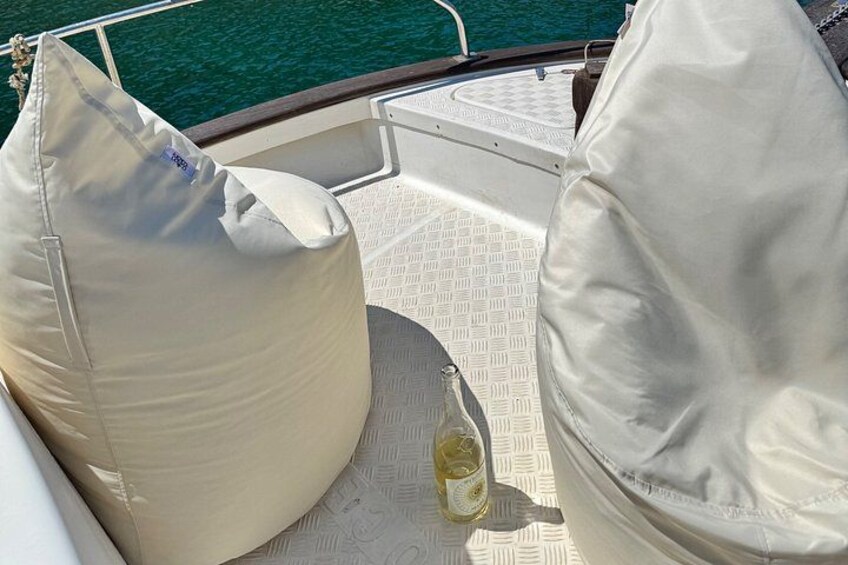 Un pont de bateau avec deux coussins de couleur beige, une bouteille de vin blanc et une rambarde en métal. 5