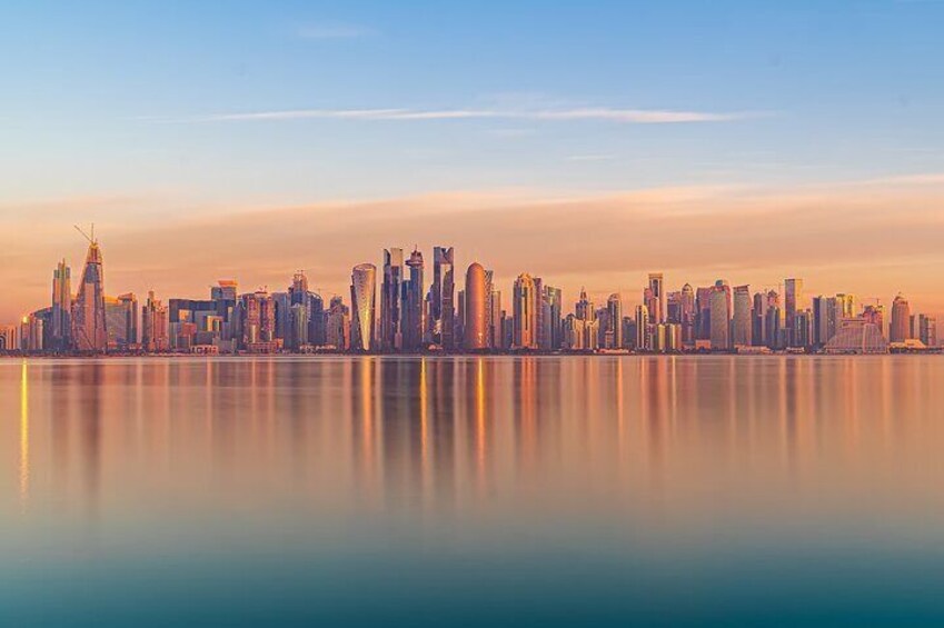 A city skyline at sunset with a calm body of water reflecting the buildings. 4