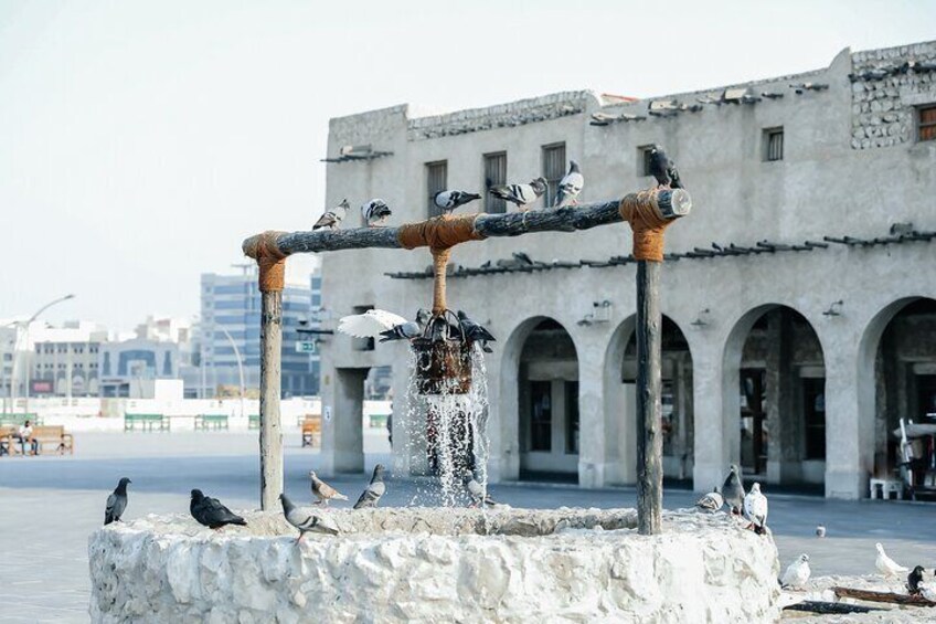 A fountain with water flowing, surrounded by pigeons, in front of a historic building with arches. 3