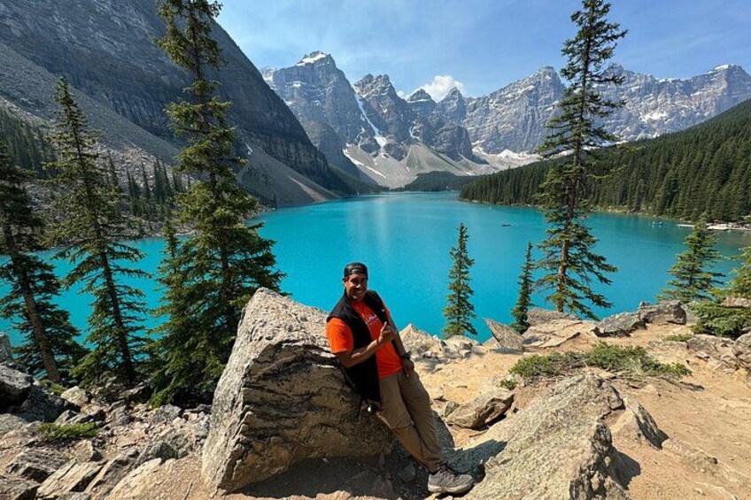 A person sitting on a rock by a turquoise lake surrounded by mountains. 3