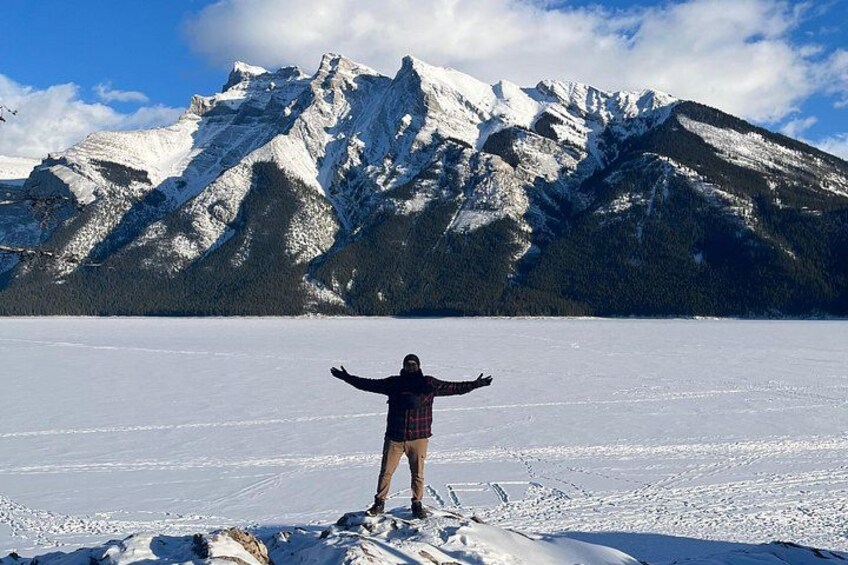 A person standing on a snow-covered peak with arms outstretched, facing a mountain range. 4