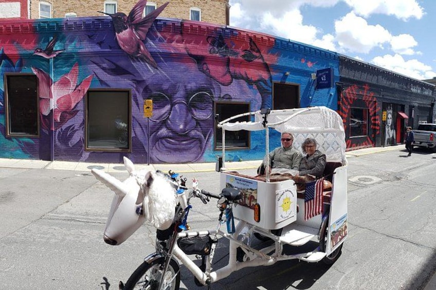 Escena callejera con un mural, un carruaje tirado por caballos blancos y un edificio con un ventanal grande. 1