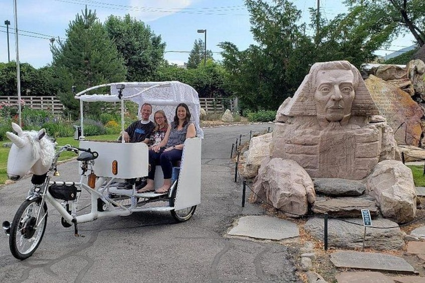 Un carruaje blanco con cabeza de caballo, dos personas y una gran escultura de piedra. 3