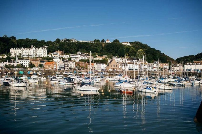 A marina with numerous boats docked, a coastal town with buildings, and a hill with greenery in the background. 3