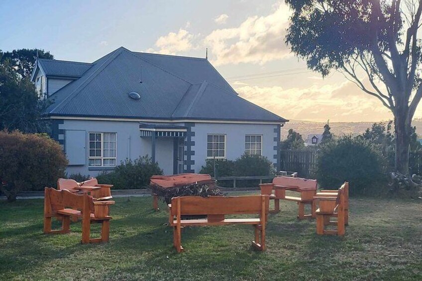 Una casa de paredes blancas y techo gris, rodeada de un césped y muebles de madera. 3