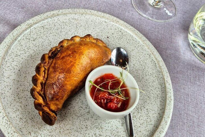 A meat pie on a speckled plate with a small bowl of red sauce and a spoon. 5