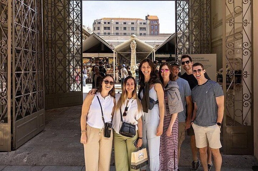 A group of people standing in front of a metal gate with a market in the background. 1