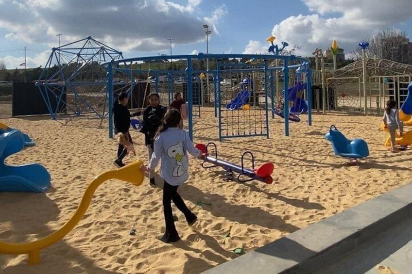 Des enfants jouent dans un parc avec du sable, des balançoires et des structures d’escalade. 1