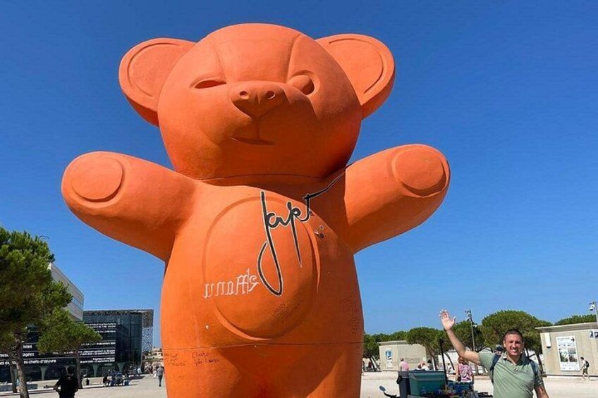 A large orange bear sculpture with a signature on its chest. 2