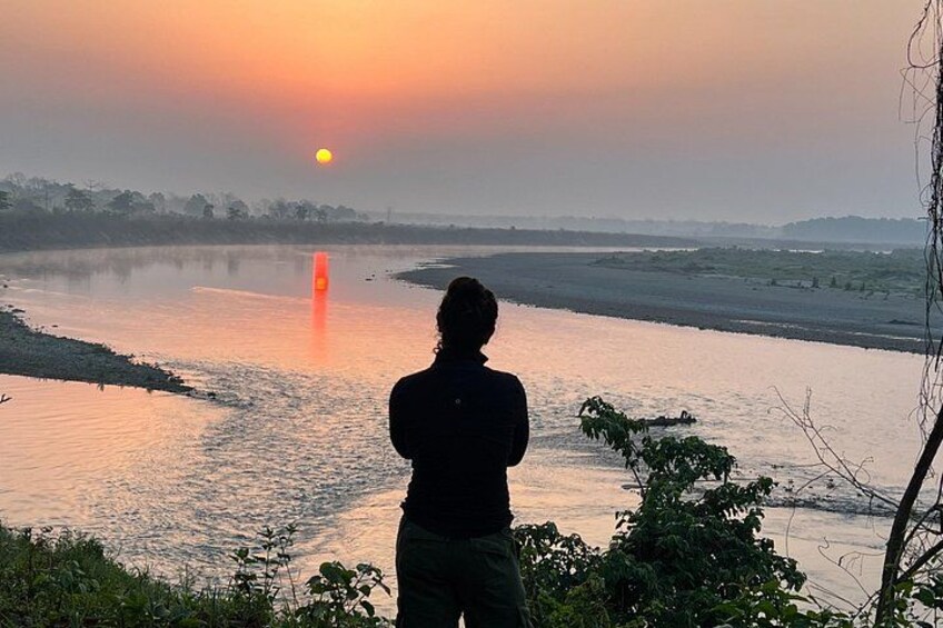 A person standing by a river during sunset. 3