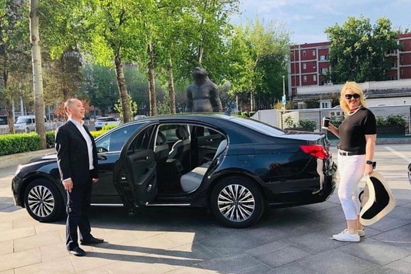 A black car parked on a paved area with trees and a statue in the background. 5