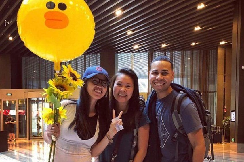 Three people in an indoor setting with a large yellow balloon, a vase with sunflowers, and a modern interior design. 3