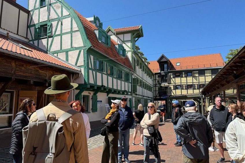 En grupp människor promenerar på en kullerstensgata i en traditionell europeisk stad med korsvirkeshus. 3
