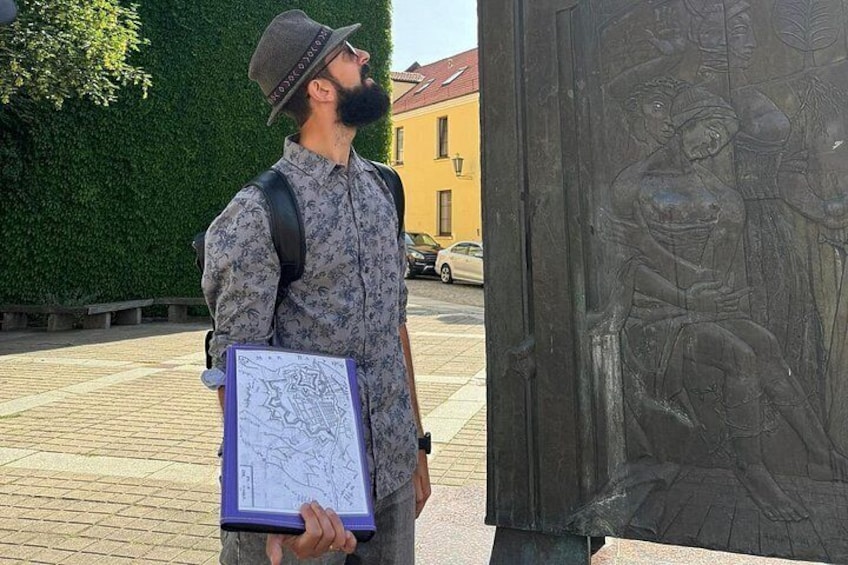 A man holding a map and standing next to a bronze sculpture. 3