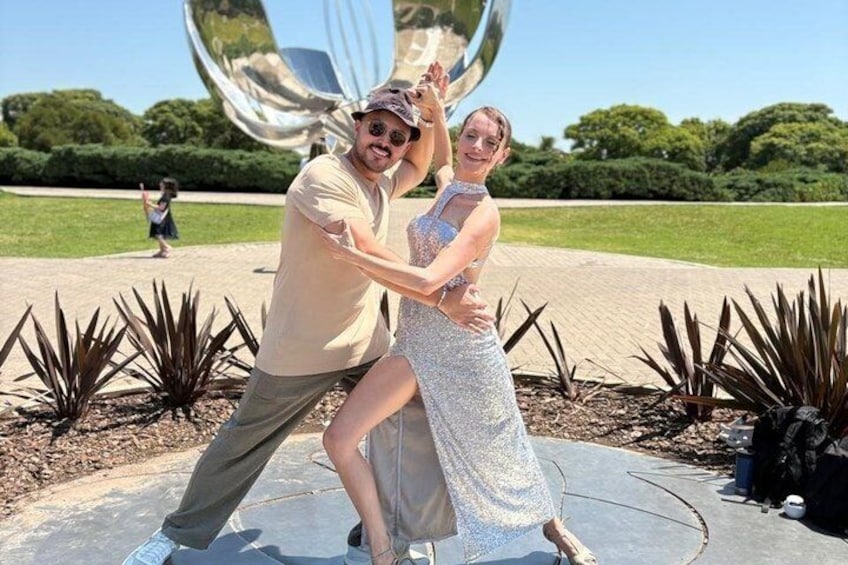 Una pareja bailando en un parque con una gran escultura reflectante al fondo. 5
