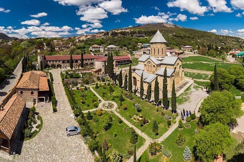 A historic church complex with a central dome, a courtyard with trees, and a mountain in the background. 5