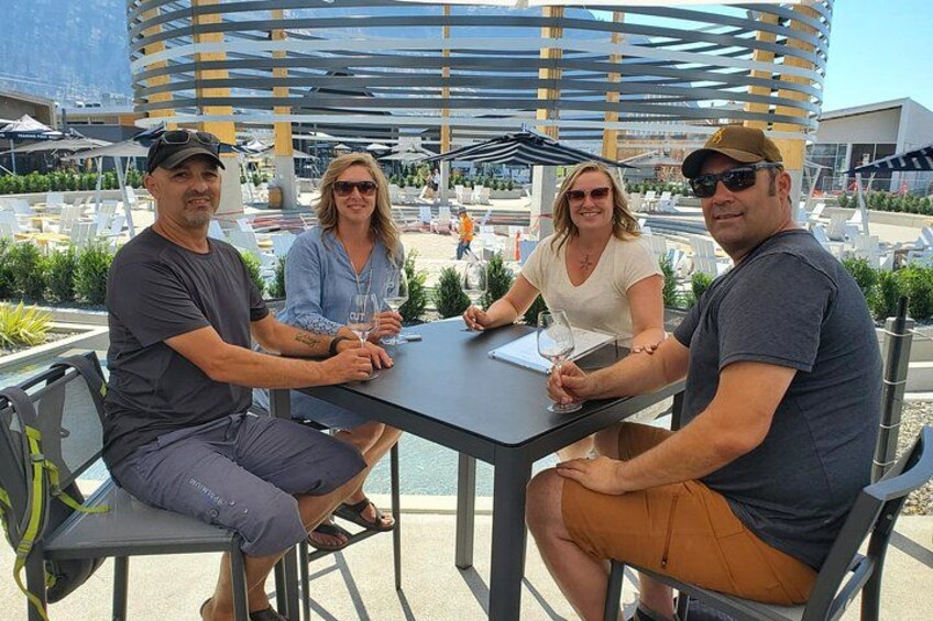 Four people seated at an outdoor table with a modern architectural background. 3