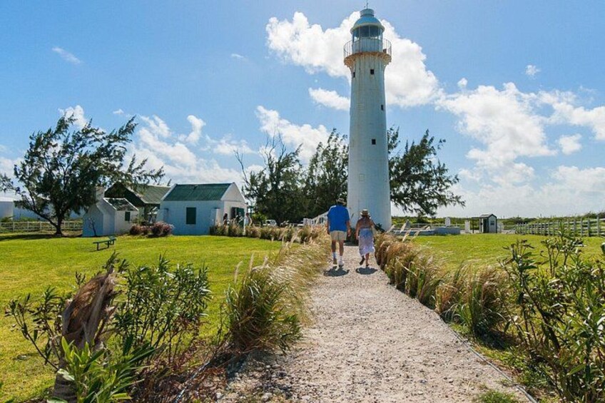 Ein Kiesweg führt zu einem weißen Leuchtturm mit grüner Kuppel, umgeben von Gras und Bäumen. 5