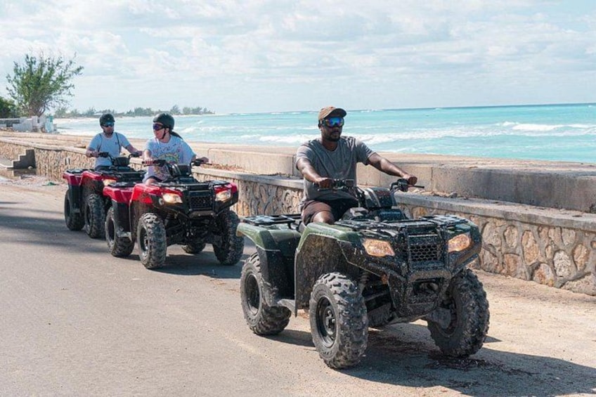 Tre personer kører på ATV'er på en kystvej med havet i baggrunden. 2