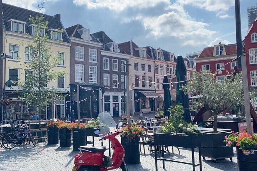 A cobblestone street with colorful buildings, outdoor seating, and a red scooter. 1