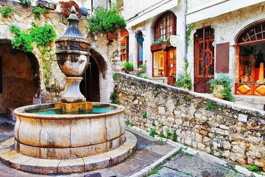 A stone fountain in a courtyard with arched windows and a stone wall. 1