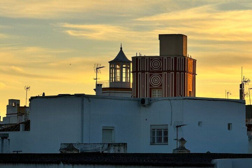 A building with a tower and a patterned structure against a sunset sky. 1