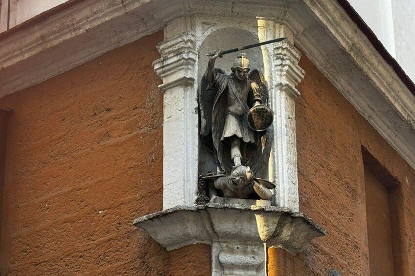 A statue of a figure holding a shield and a spear, mounted on a column with a textured wall in the background. 4