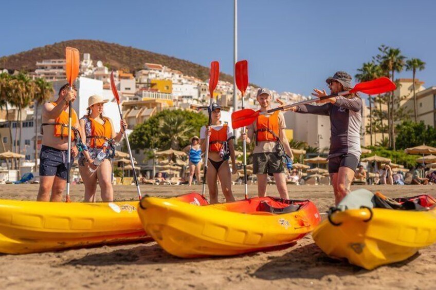 People in yellow kayaks on a beach with buildings in the background. 4