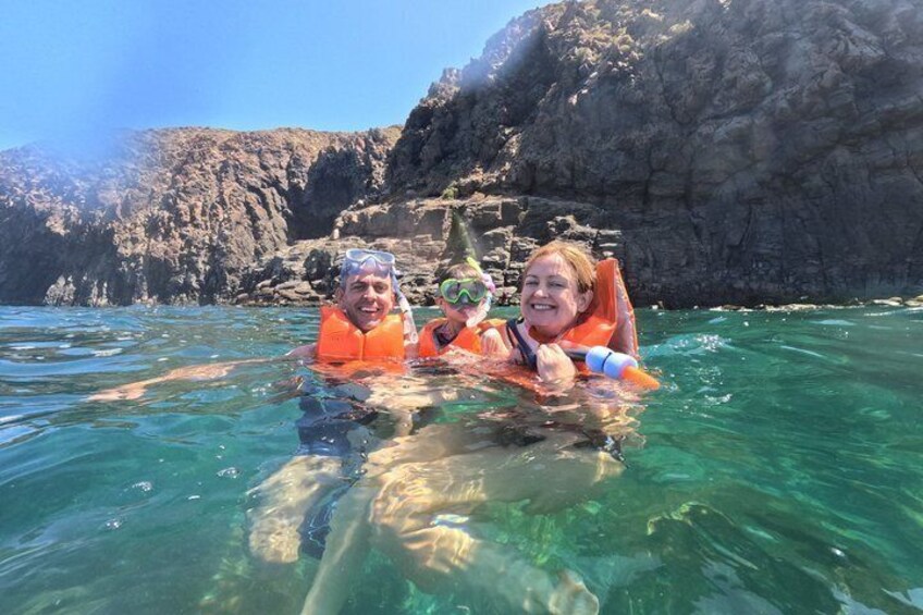 Two people in clear water with rocky cliffs in the background. 2