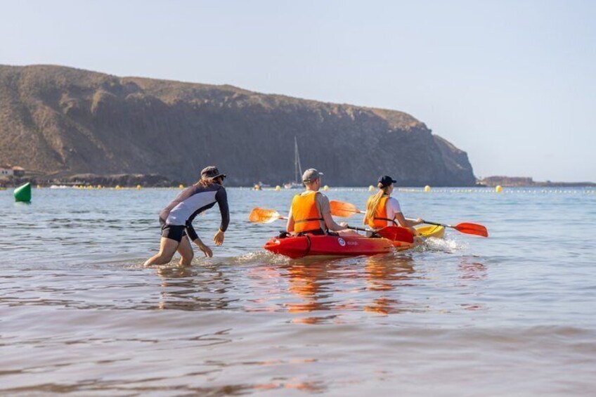 Three people kayaking on calm water with a rocky coastline in the background. 3