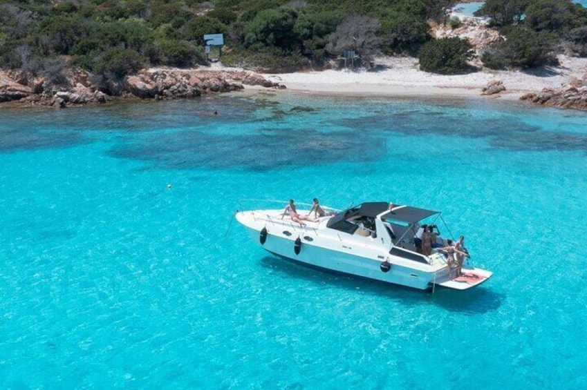 A white boat with passengers on a turquoise sea, surrounded by rocky coastline and sparse vegetation. 1