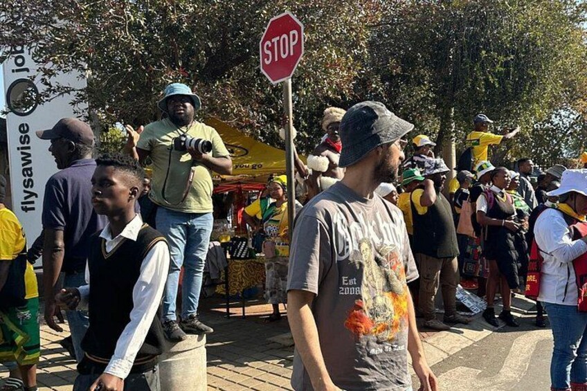 A public gathering with a stop sign, people standing, and a vendor with a yellow tent. 5