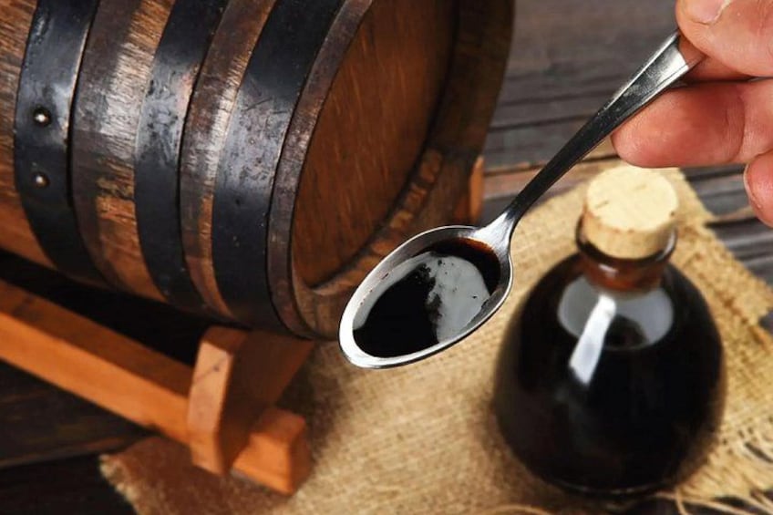 A wooden barrel with a metal band, a wooden spoon with a dark liquid, and a small bottle with a cork. 4