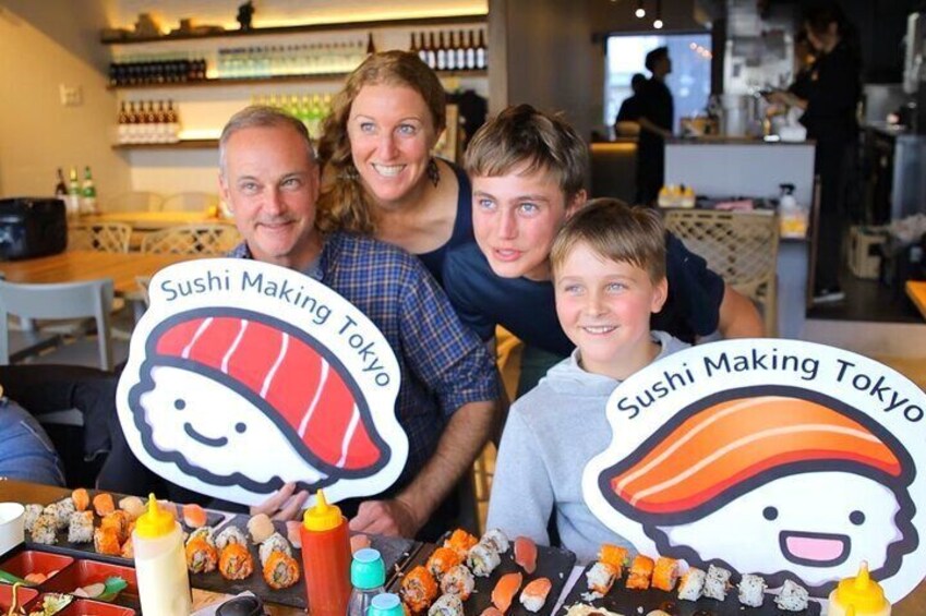 Una familia participa en un evento de preparación de sushi, con una mesa repleta de sushi y botellas de salsa. 1