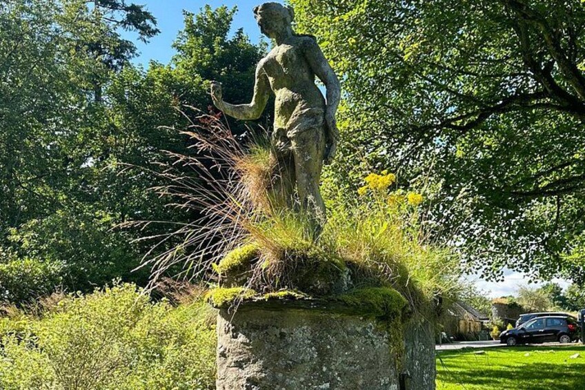 A statue of a figure with a bird, surrounded by greenery and trees. 3