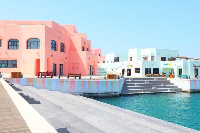 A waterfront promenade with pastel-colored buildings, a wooden walkway, and a clear blue sky. 2