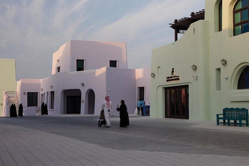 A white building with arched doorways and a green bench. 5