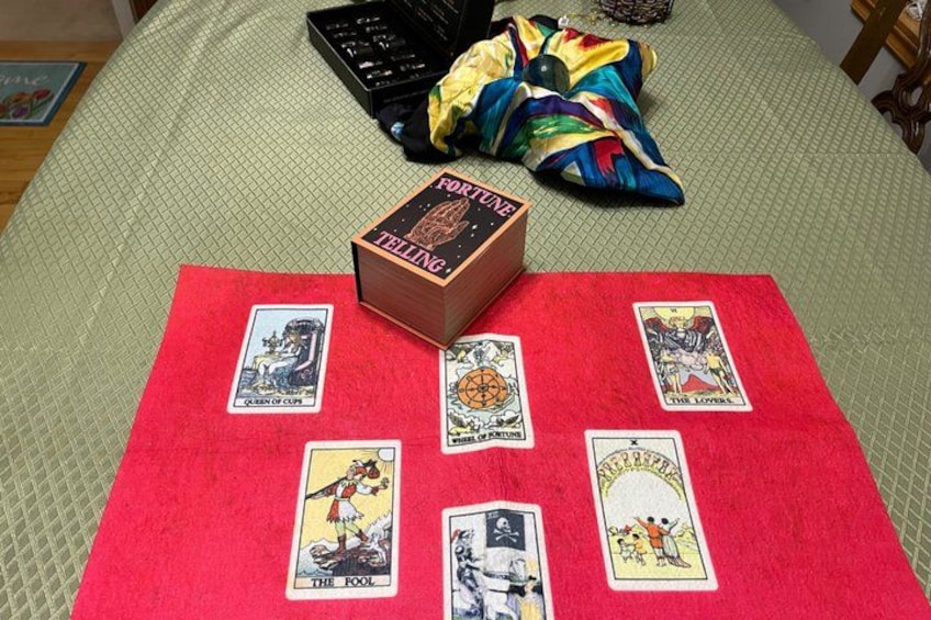 Eine Tarot-Kartenlegung auf einem Bett mit rotem Tuch, einer Box mit der Aufschrift 'FORTUNE TELLING' und einer farbenfrohen Decke. 2