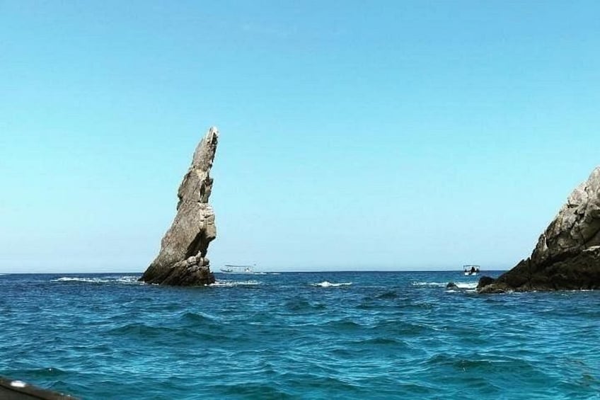 A coastal scene with a prominent rock formation in the water and a boat in the distance. 2