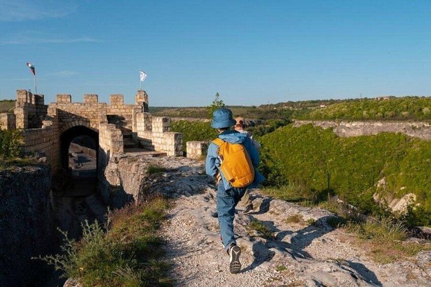 A person hiking on a rocky path with a historical stone structure in the background. 2