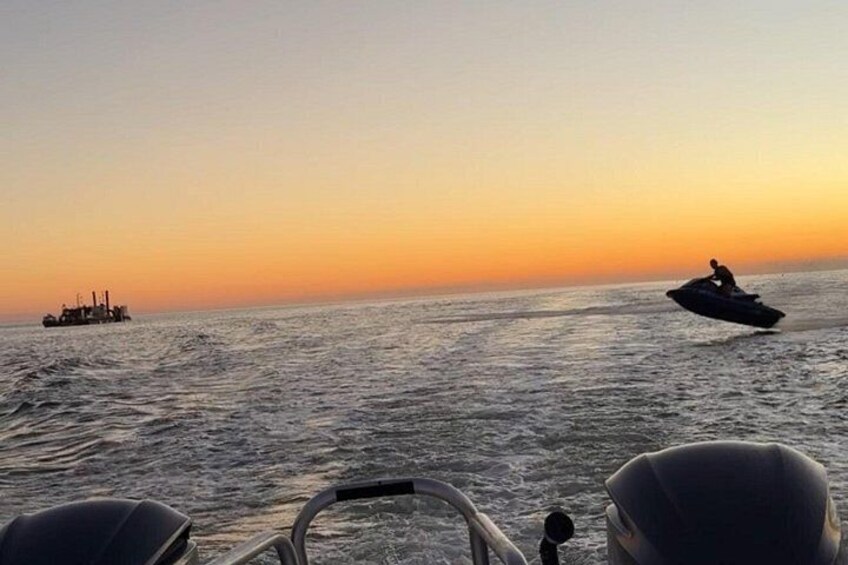 A jet ski on the water, a boat in the distance, and a sunset. 4