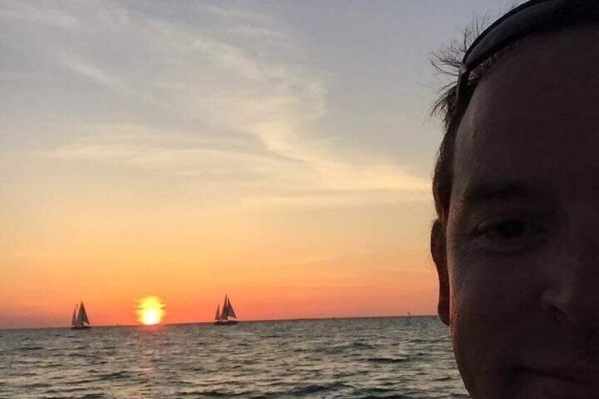 A sunset over the ocean with two sailboats. 2