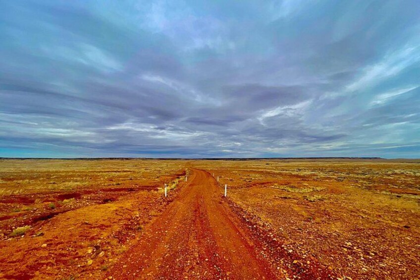 A dirt road in a barren landscape with a cloudy sky. 2