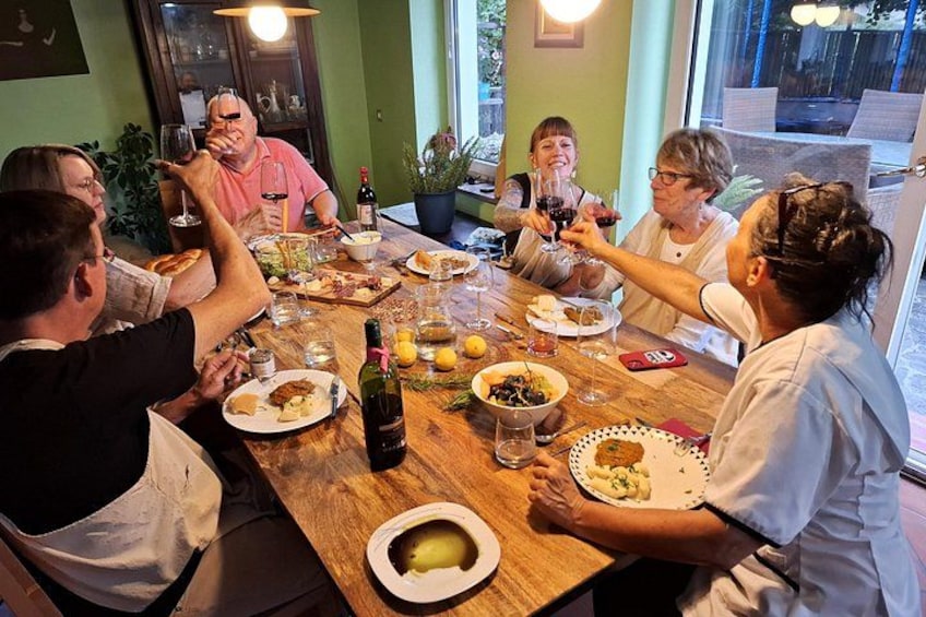 A group of people sitting around a wooden table, toasting with wine glasses. 1