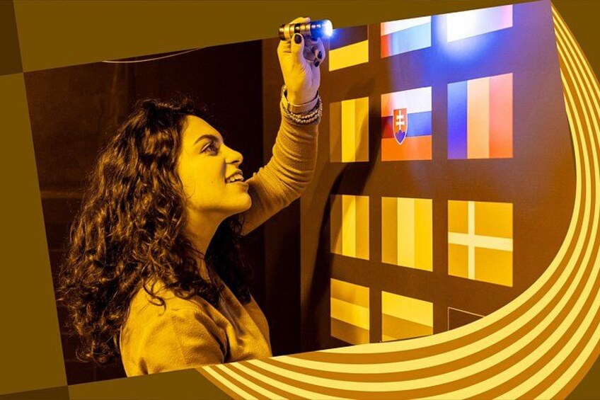 A person holding a light source towards a wall with illuminated flags. 2