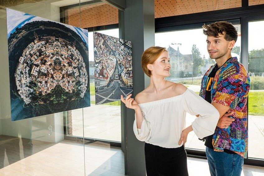Two people standing indoors, looking at large circular artworks on glass panels. 5