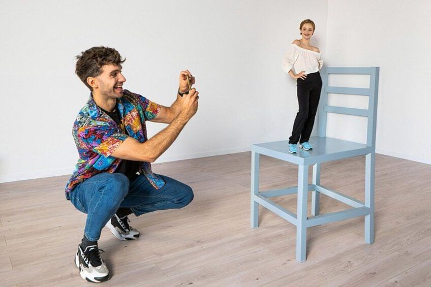 A person crouching and taking a photo of another person standing on a blue chair. 3