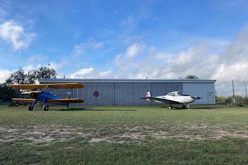 Two airplanes parked on a grassy field with a hangar in the background. 5